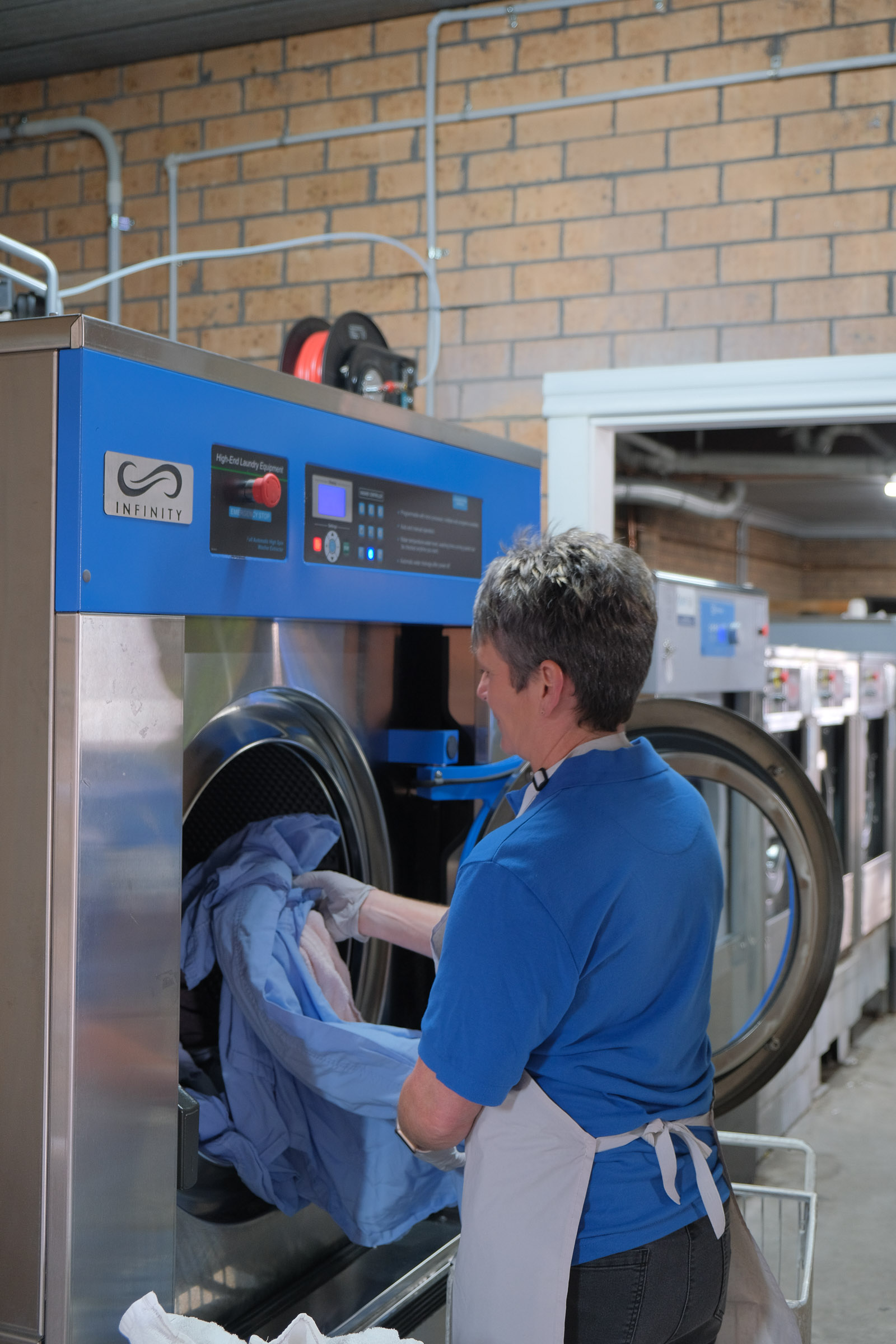 A commercial laundry worker loading hospital gowns into a large front loading washer